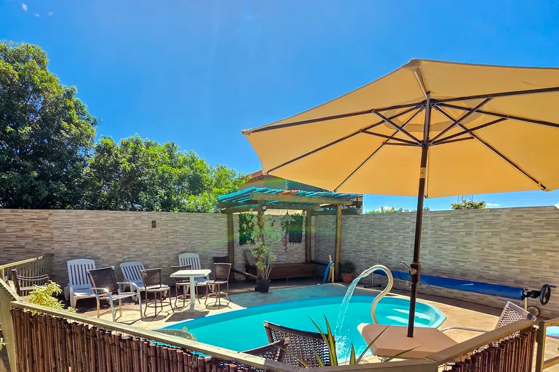 Piscina da pousada ao sol, com guarda-sol e espreguiçadeiras